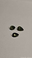 Three pear-cut green sapphires displayed on white background under neutral light, showing size and color.