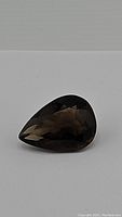 Pear cut natural smokey quartz gemstone photographed on gray surface showing color and faceting detail.