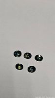 Five oval-shaped sapphires with tri-color tones under normal lighting showing their color variety and luster.
