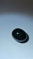 Oval cabochon Jet Black Ethiopian opal displaying green flashes under a focused light.