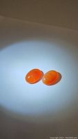 Pair of natural mandarin fanta orange carnelian gemstones shown under light, oval shape, smooth polished surface.