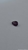 Pear-shaped faceted purple pink sapphire gemstone photographed against grey background to show color and shape.