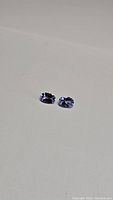 Two natural untreated tanzanite gemstones displayed on white background, showing color and cut.