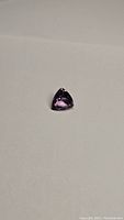 Natural purple pink amethyst gemstone, trillion cut, placed on plain background showing shape and color.