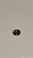 Close-up photo of the oval cut pink purple sapphire showing the color and facets on a neutral background.