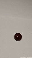 Deep red round carnelian cabochon on white background under normal light, showing glossy surface and uniform color.