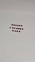 Top view photo showing 22 small round faceted rubies arranged in two neat rows on a white background. Stones exhibit deep red to pink coloration.