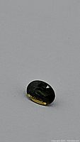 Oval cut sapphire showing mostly dark appearance with subtle yellow flashes under diffused lighting.