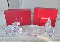 Three crystal sculptures displayed with two red Baccarat boxes