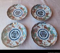 Four antique Japanese ornate plates arranged on cloth surface showing overall condition and design