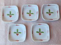 Five small square white porcelain plates with hand-painted red radish and green leaves design, featuring red wavy line accents on the edges, arranged on a fabric background.