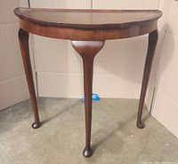 Front view of the antique half moon console table showing curved legs and raised edge top