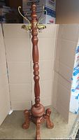 Full view showing entire tall wooden coat rack with brass hooks and ornate base.