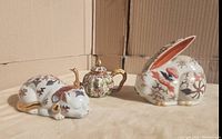 Photo shows all three items: the cloisonne teapot with dragon handle, the sleeping cat figurine, and the bunny figurine placed together on a surface.