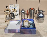 All 5 coffee items displayed together on a surface, including two boxed French presses, one unpackaged French press and two vintage carafes with metal construction.