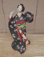 Front and left side view of hand-painted Hakata Geisha doll wearing black floral kimono, posed in traditional dance gesture.