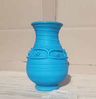 Front view of bright blue art glass vase with horizontal ridges and abstract raised circular decorations, certificate visible beside it.