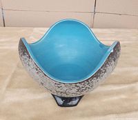 Front view of blue interior and textured exterior on ceramic bowl with three-legged base.