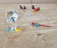 Overview of all items including large faceted crystal diamond, two colorful Murano glass roosters, Baccarat crystal dog, pink crystal heart with two small birds, Murano glass mouse, and two Swarovski figurines