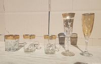 Front view of the complete lot showing all five crystal glasses in a row on a white surface, highlighting gold gilded rims and decorative features.
