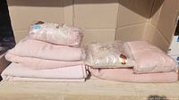 Pink blankets stacked with three sealed decorative pillows, two featuring Victorian style ornate patterns, faux pearls, and cameo elements