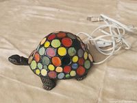 Angle shot showing the turtle lamp with colorful round stained glass pieces on its shell, attached to the electrical cord.