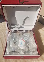 Two Timon crystal wine glasses with silver gilded rims inside red box lined with white satin fabric. Certificate of authenticity card visible.
