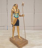 Full view of golden Ra statue standing on rectangular base with hieroglyphs, holding staff and ankh.