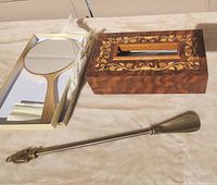 Photo showing the ornate wooden tissue box with floral inlay, brass shoe horn with horse head handle, and hand painted Japanese hand mirror with gold frame.