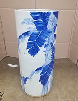 Front and side views of tall cylindrical porcelain umbrella stand with blue foliage painted on white glaze.