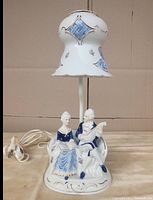 Front view showing porcelain figurines of a man and woman seated, supporting the porcelain shade with floral and blue basket weave designs.