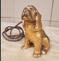 Front view of the vintage brass seated dog with woven leather leash attached.