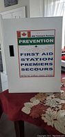 Front view of the white powder-coated first aid cabinet with a label 'First Aid Station' showing Canadian flag and text.