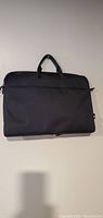 Black nylon laptop sleeve with top carry handles displayed flat against wall.