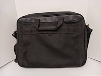 Front view of the black laptop tote bag with handles and a clean solid surface.