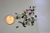 58 loose small rectangular multi-colored tourmaline gems displayed next to a penny for size reference.