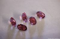 Five small oval cut pink tourmaline loose gemstones arranged on a flat surface.