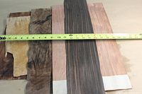Five exotic wood veneer sheets laid side by side with measuring tape showing approximate length around 15 inches.