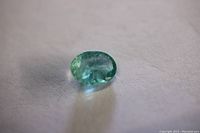 Light green oval cut emerald loose gemstone on a light background, showing facets and transparency with internal inclusions visible.