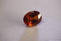 Oval cut orange garnet loose gemstone on white surface, showing front facets and glow