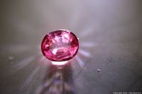 Clear top view of the loose peach sapphire oval cut gemstone with visible internal facets and pinkish color tone.