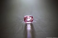 Single loose pink spinel gemstone, cushion cut, placed on a reflective surface showing the top view with pink hue and light reflections.