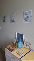 Photo showing art wall with three framed artworks above a dresser with ceramic ginger pot, glass candle holder, decorative book, and framed pictures