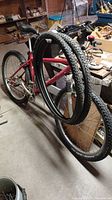Red mountain bike with extra tires hung on frame in workshop.