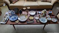 Long shot of all items arranged on mid-century style wood bench showing variety of china, glass, candlesticks and decorative items