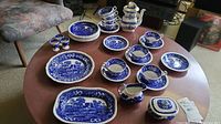Full view of the 28-piece Copeland's Spode Tower china set laid out on table, showing various cups, saucers, plates, teapot, creamer, sugar bowl with blue and white pastoral design.