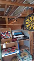 Wide shot of shelving unit holding Lego box, toy trains, and metal vehicles, with dartboard in background
