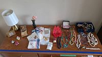 Overview of entire lot on wooden surface showing lamp, clock, costume jewelry, handkerchiefs, and small floral items