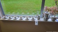 Full set on window sill: five tea cups with matching saucers plus creamer and sugar bowl, all porcelain with floral pattern and gold rims.