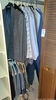 Closet view showing hanging blazers, dress shirts, and pants in various patterns and colors